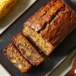 A slice of Janet's Rich Banana Bread with walnuts and bananas on a wooden cutting board.